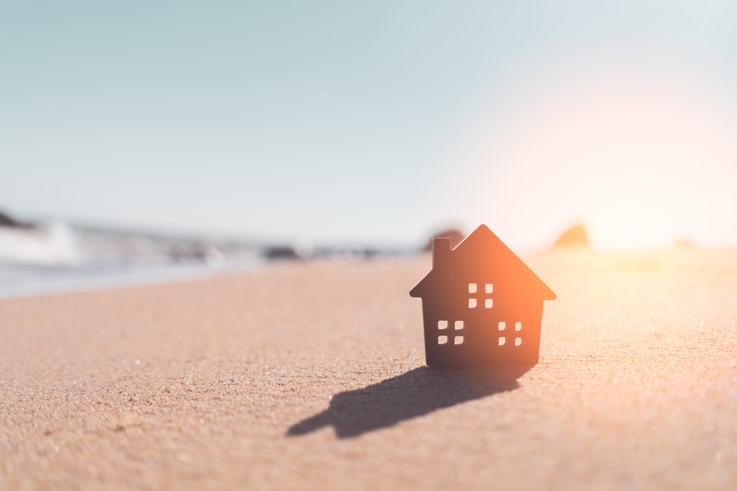 Small home model on sunset beach sand texture background. Copy space of family lifestyle and business real estate concept. Vintage tone filter effect color style.